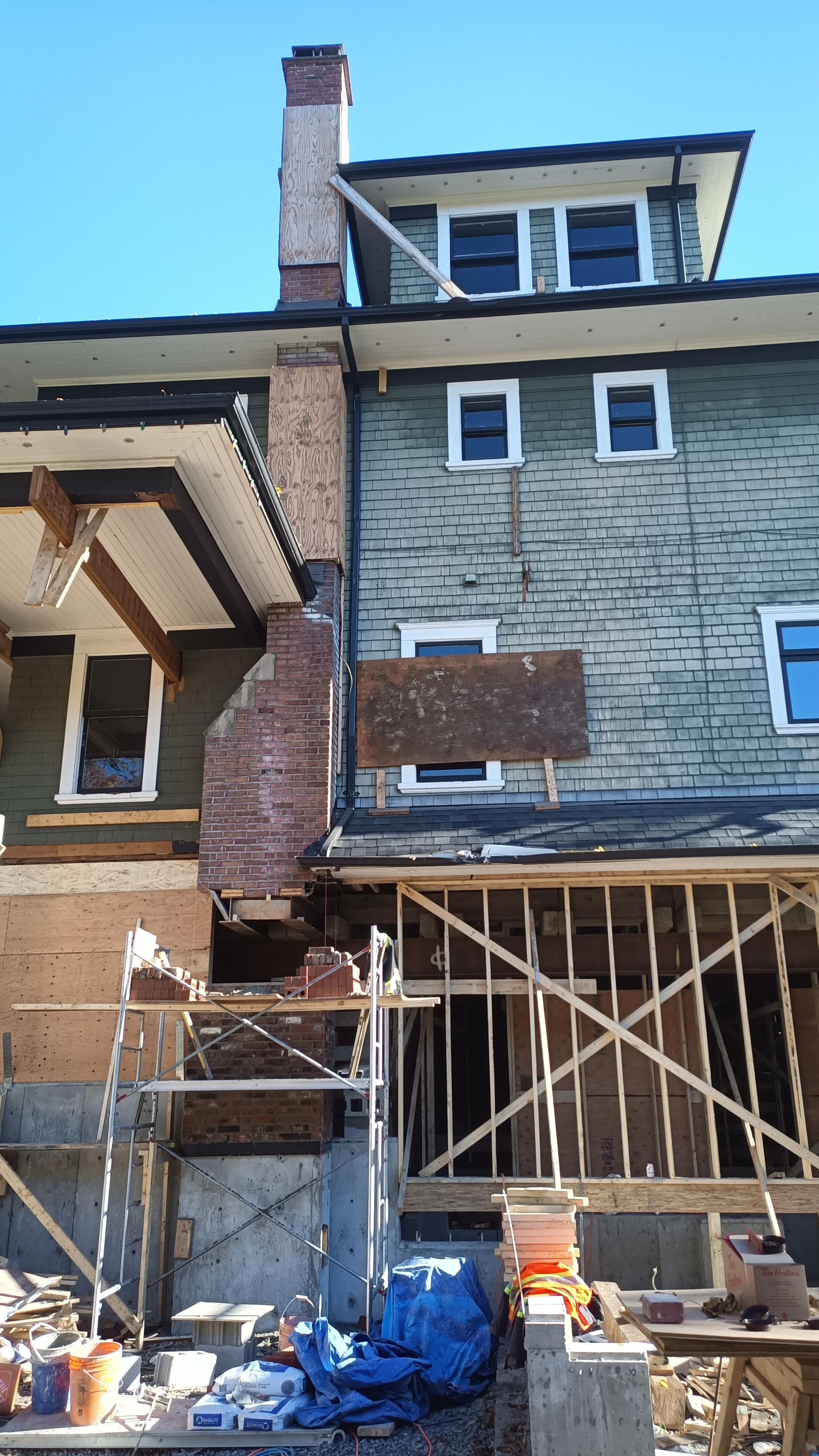 Renovation site with house exterior scaffolded and exposed framing, blue tarp and construction materials below