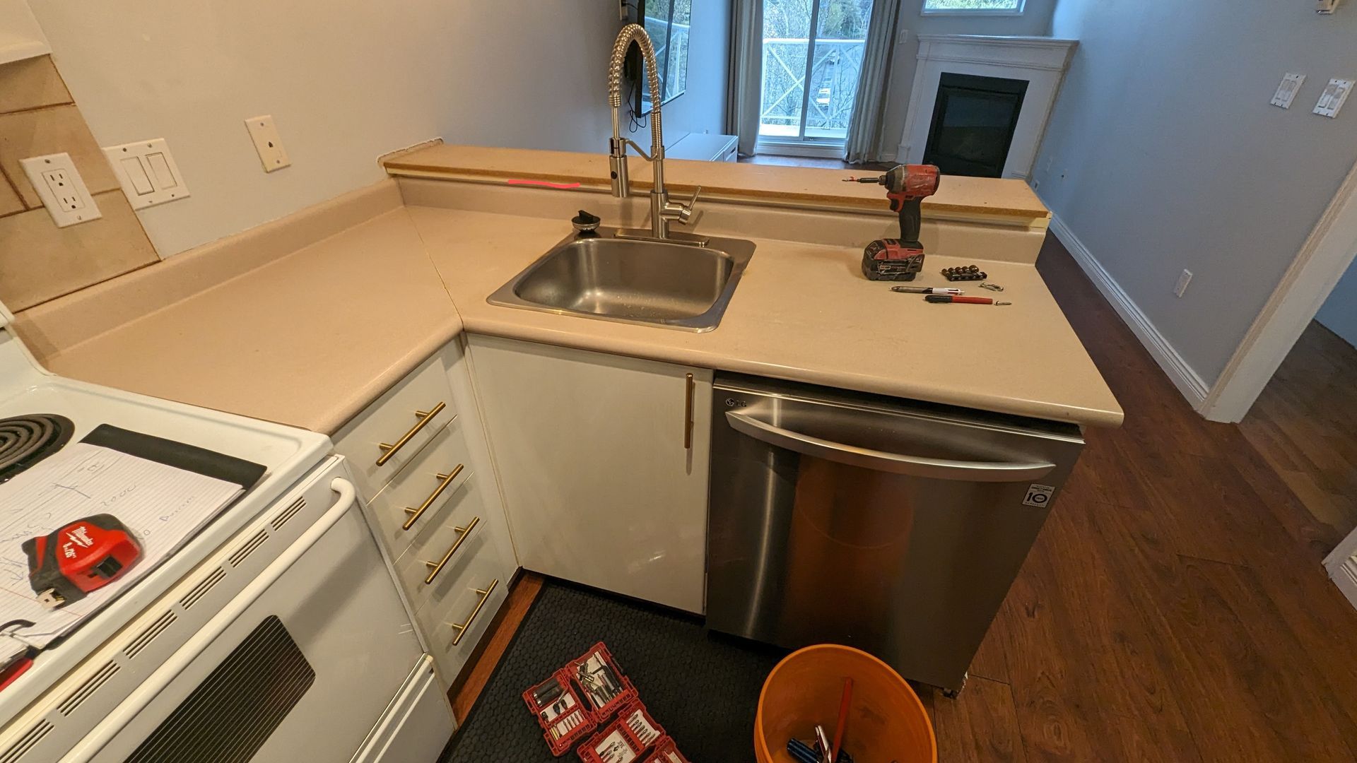 Small kitchen with sink, stainless dishwasher, white stove, countertops, and a drill near the window.