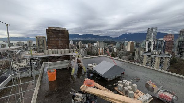 Rooftop construction site with tools and debris, overlooking a cloudy city skyline and mountains.