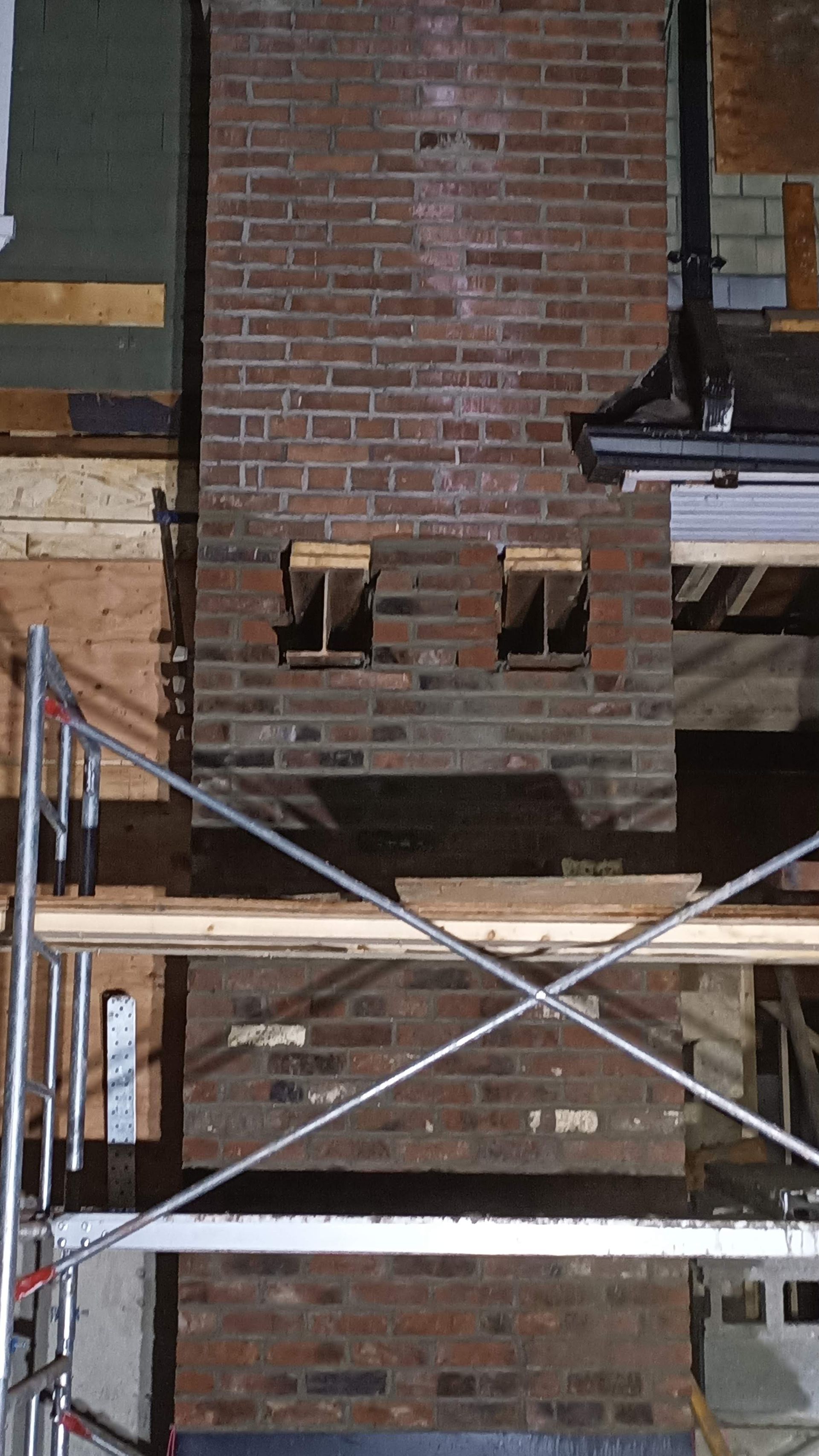 Brick wall under construction with scaffolding and exposed openings.
