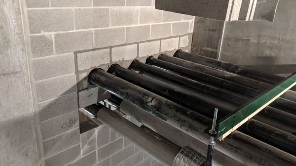 Black pipes entering a gray cinder block wall in an industrial setting