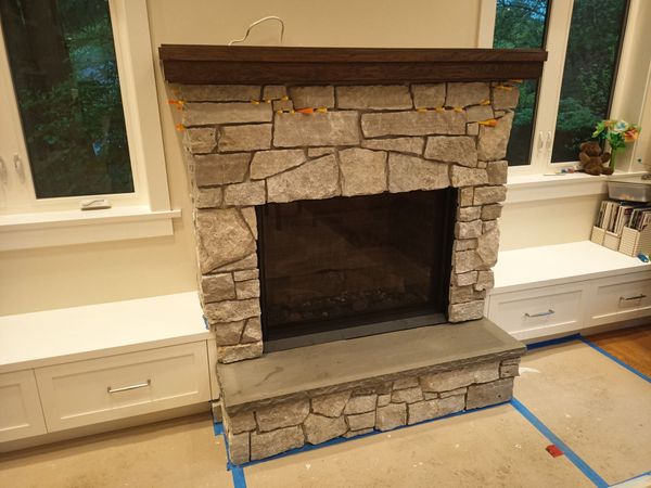 Stone fireplace with dark firebox and built-in white cabinets in a room under renovation