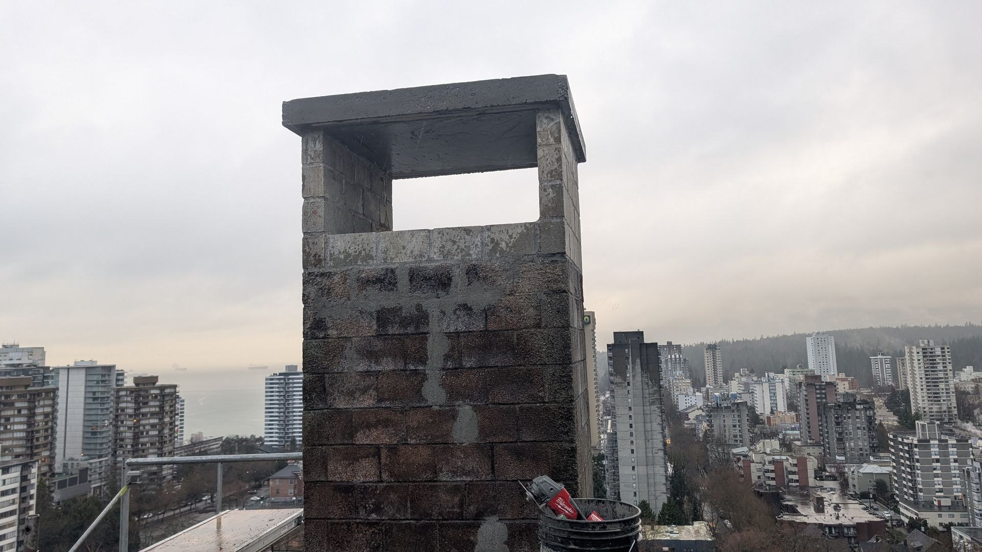 A repaired chimney on top of a building with the city of Vancouver in the background.