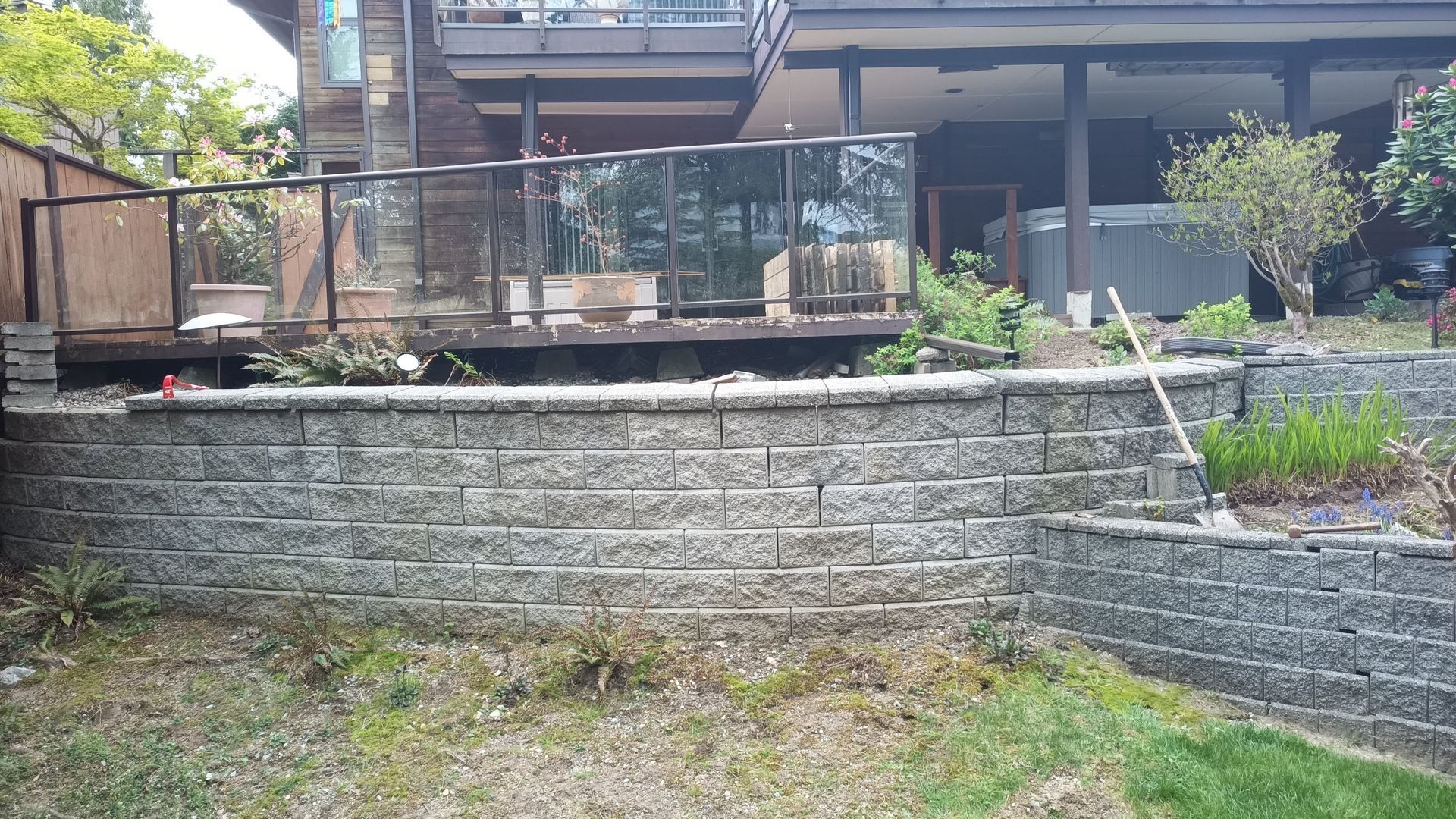 Backyard patio with stone retaining wall, plants, and a covered deck above a grassy yard