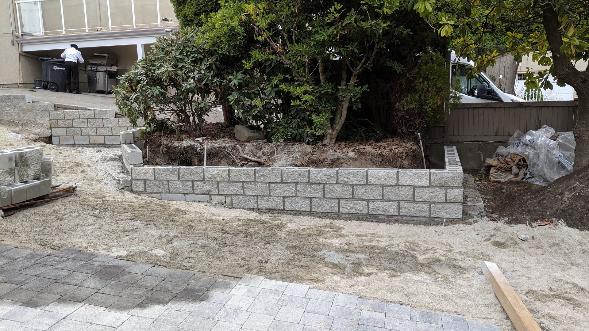 Stone retaining wall and terraced garden beside a driveway with piles of gravel and construction debris.