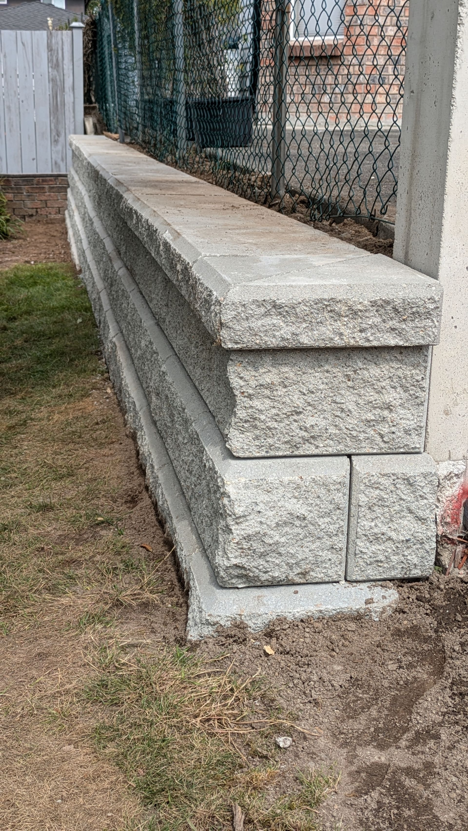 Stacked concrete retaining wall blocks beside a chain-link fence on a grassy yard