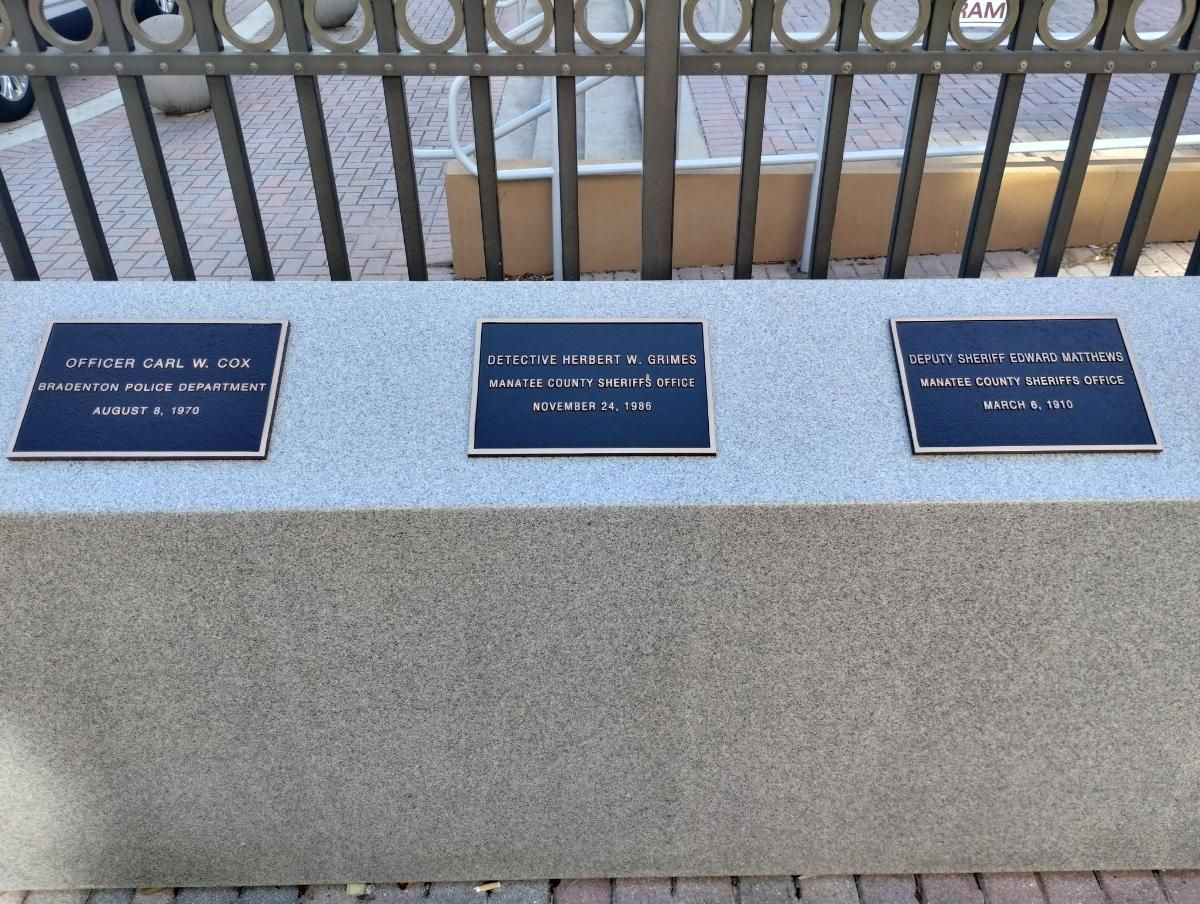 A bench with three plaques on it and a fence in the background