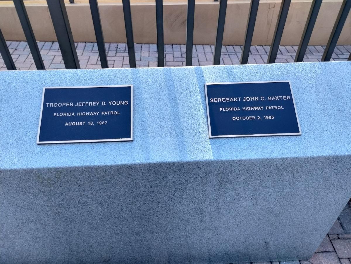 Two blue plaques on a concrete bench with a fence in the background