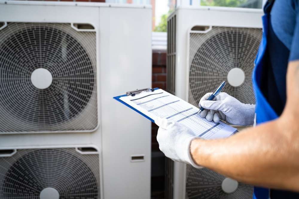 Technician in blue shirt checking an HVAC unit and writing on a clipboard outdoors