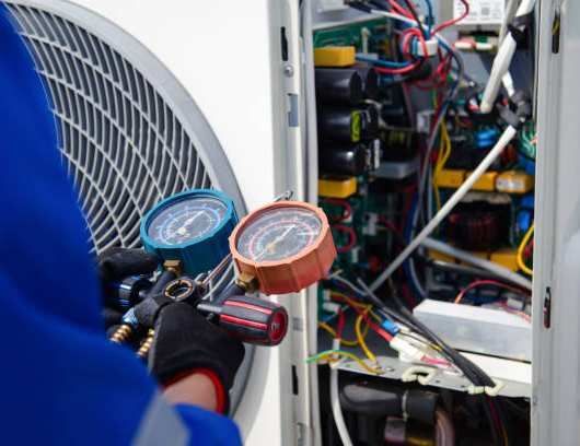 Technician checking HVAC gauges beside an outdoor air conditioner unit and open electrical panel.