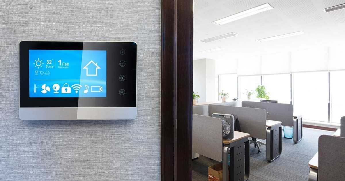Wall-mounted touchscreen in a bright office meeting room, showing a blue home-control interface.
