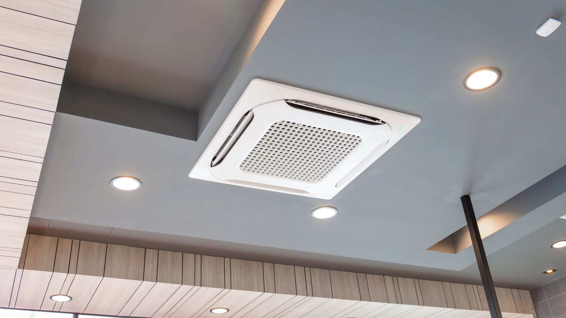 Ceiling-mounted air conditioner in a modern interior with recessed lights and a gray ceiling