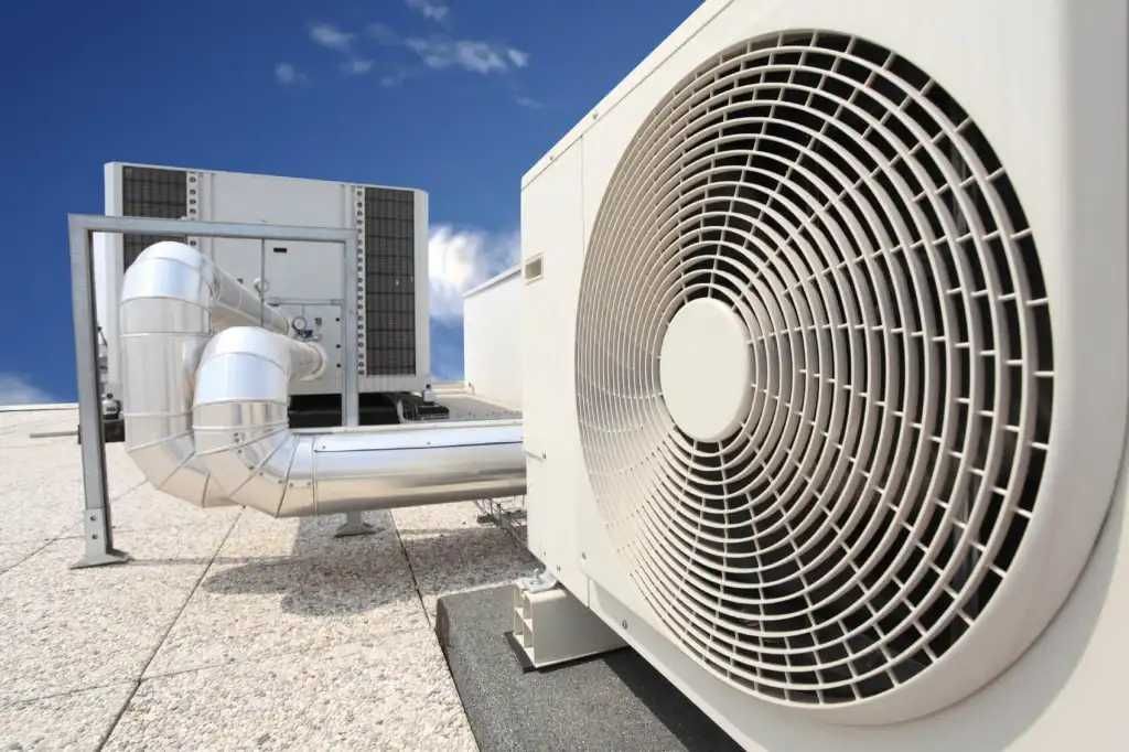 Rooftop HVAC units with large circular fans and metal ductwork under a bright sky