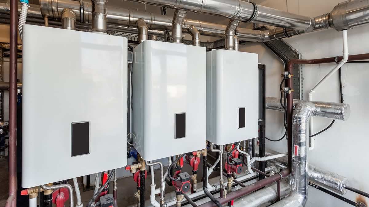 Three white wall-mounted boilers with pipes and valves in a utility room