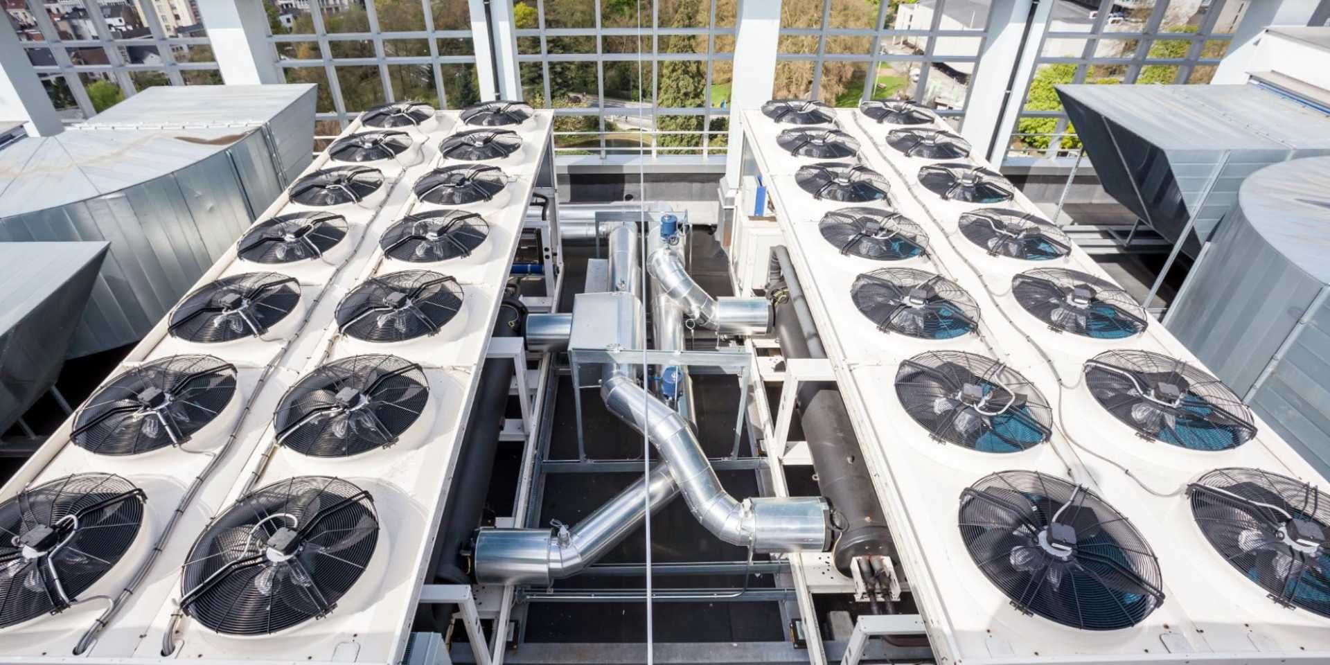 Rooftop HVAC units with large fans and metal ductwork between white building sections