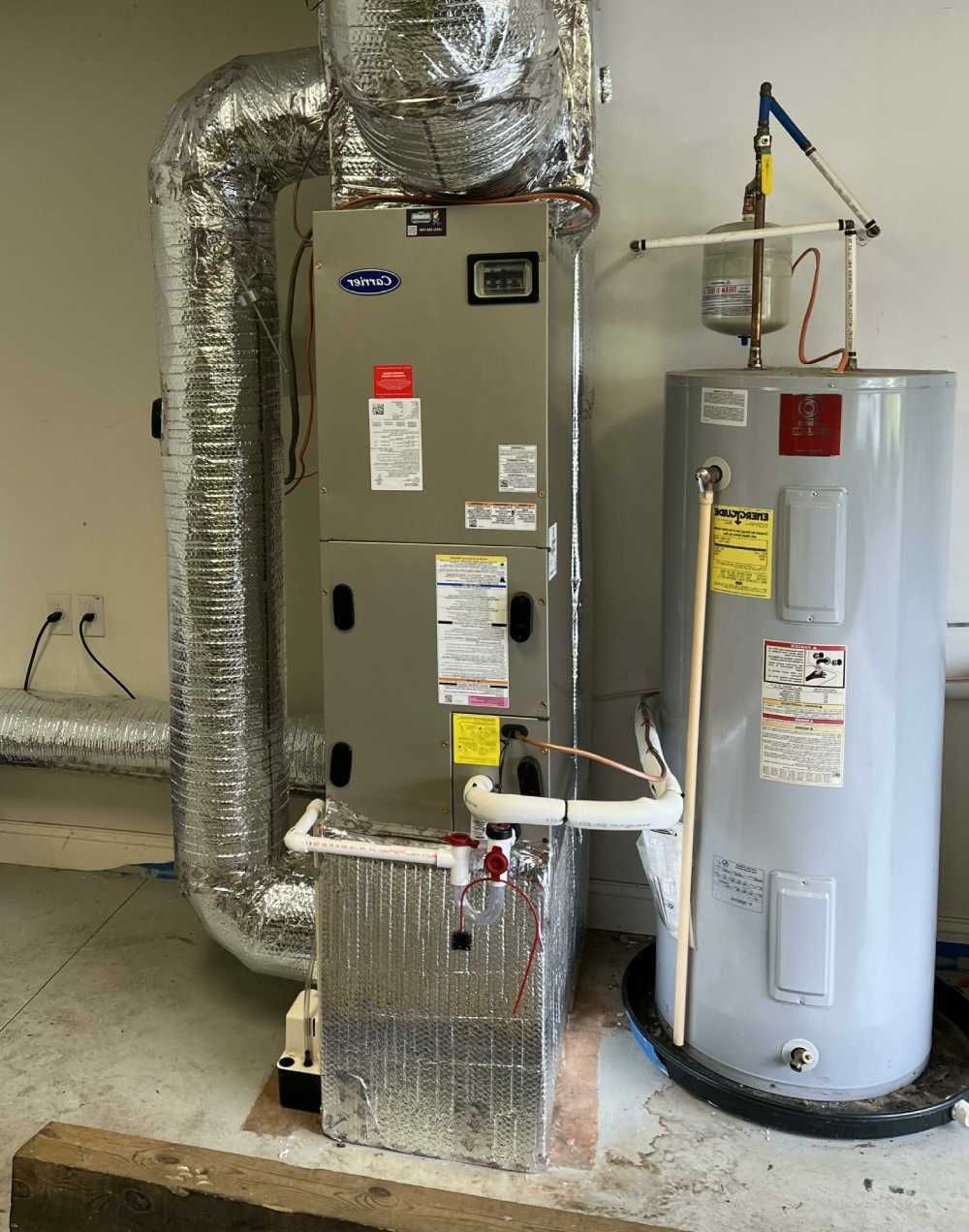 Furnace and water heater in a utility room with exposed ductwork and pipes.