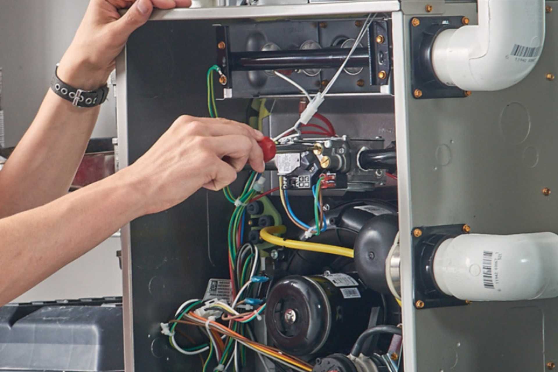 Technician wiring an open HVAC unit, with colored cables and pipes visible inside the metal panel.