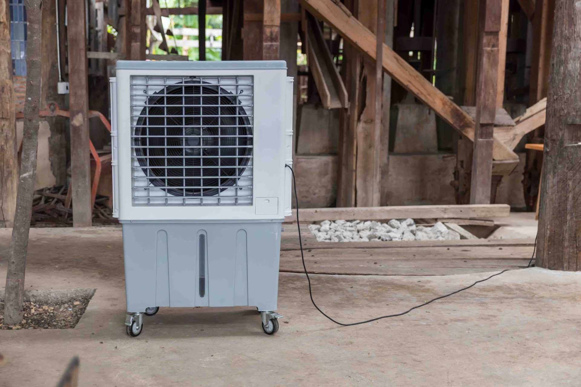 Portable gray evaporative cooler on wheels in a rustic wooden shed, with a power cord attached