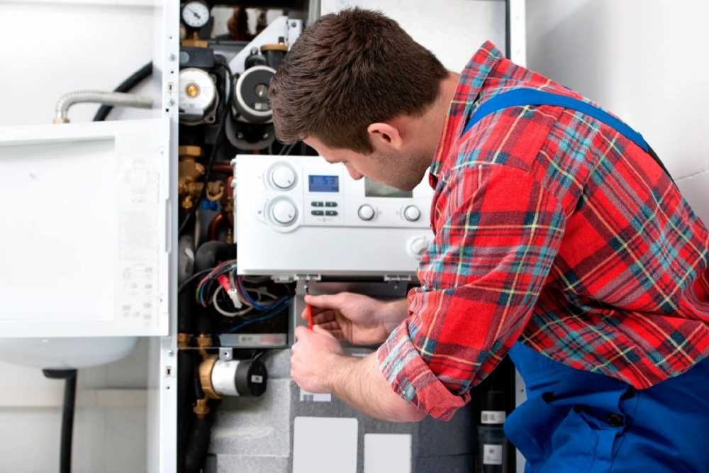 Technician in red plaid shirt inspecting a boiler unit with tools in a utility room