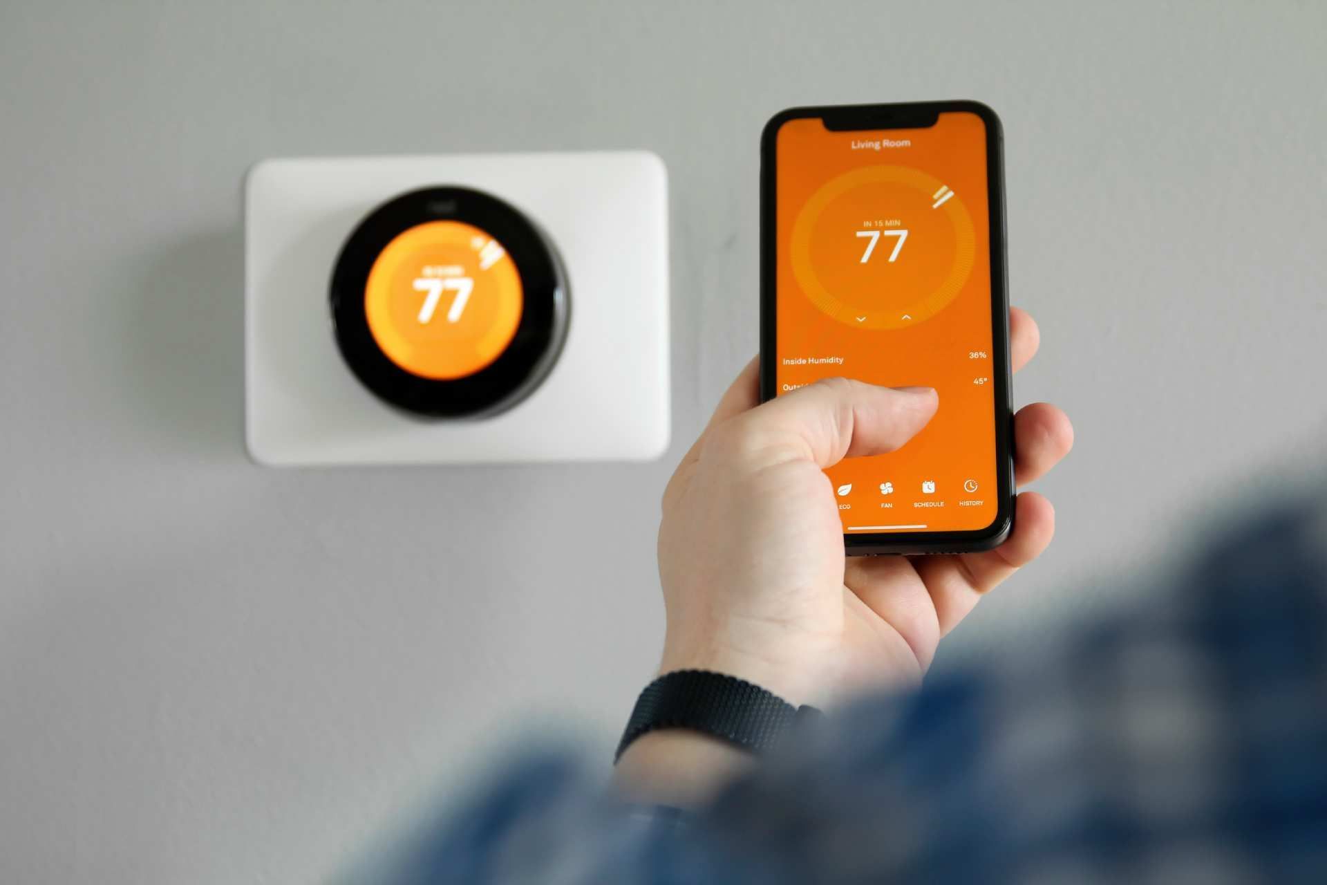 Person adjusting a smart thermostat to 77° with a smartphone app