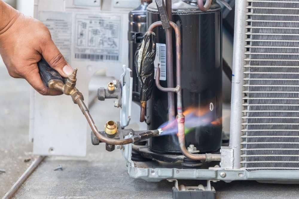 Technician using a torch to braze a metal HVAC compressor component