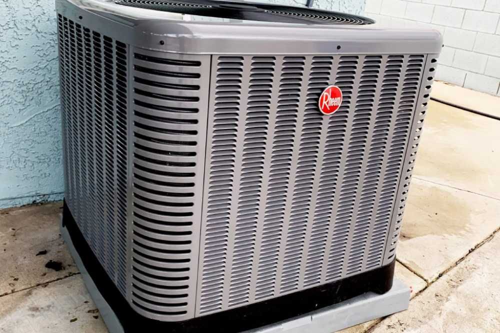 Outdoor central air conditioning unit with gray grille and red logo on a concrete pad.