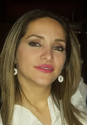 Woman with long hair, wearing earrings and a white top, looking at the camera with a slight smile.