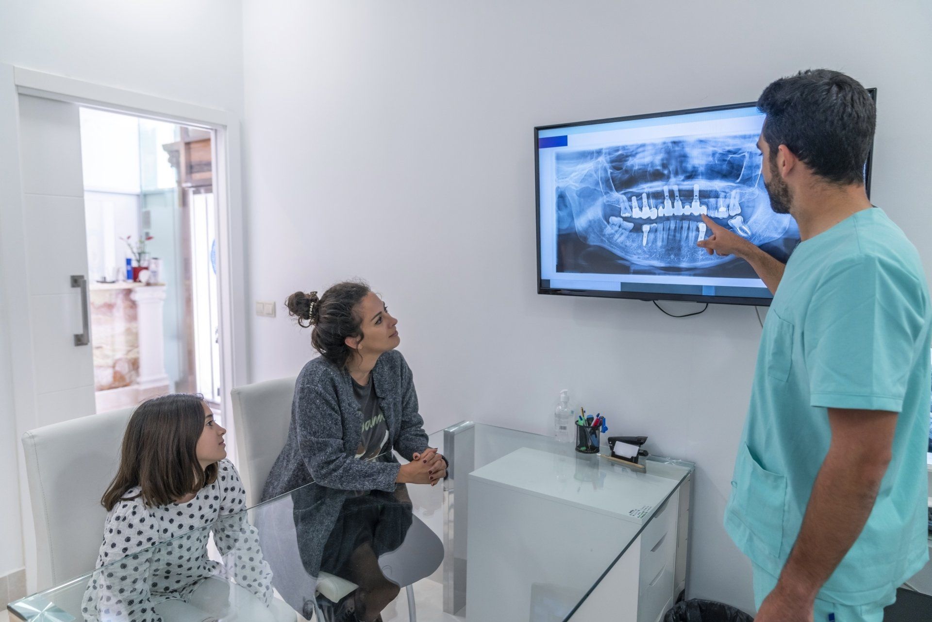 Dentist showing dental X-ray to a patient and child in a bright office.