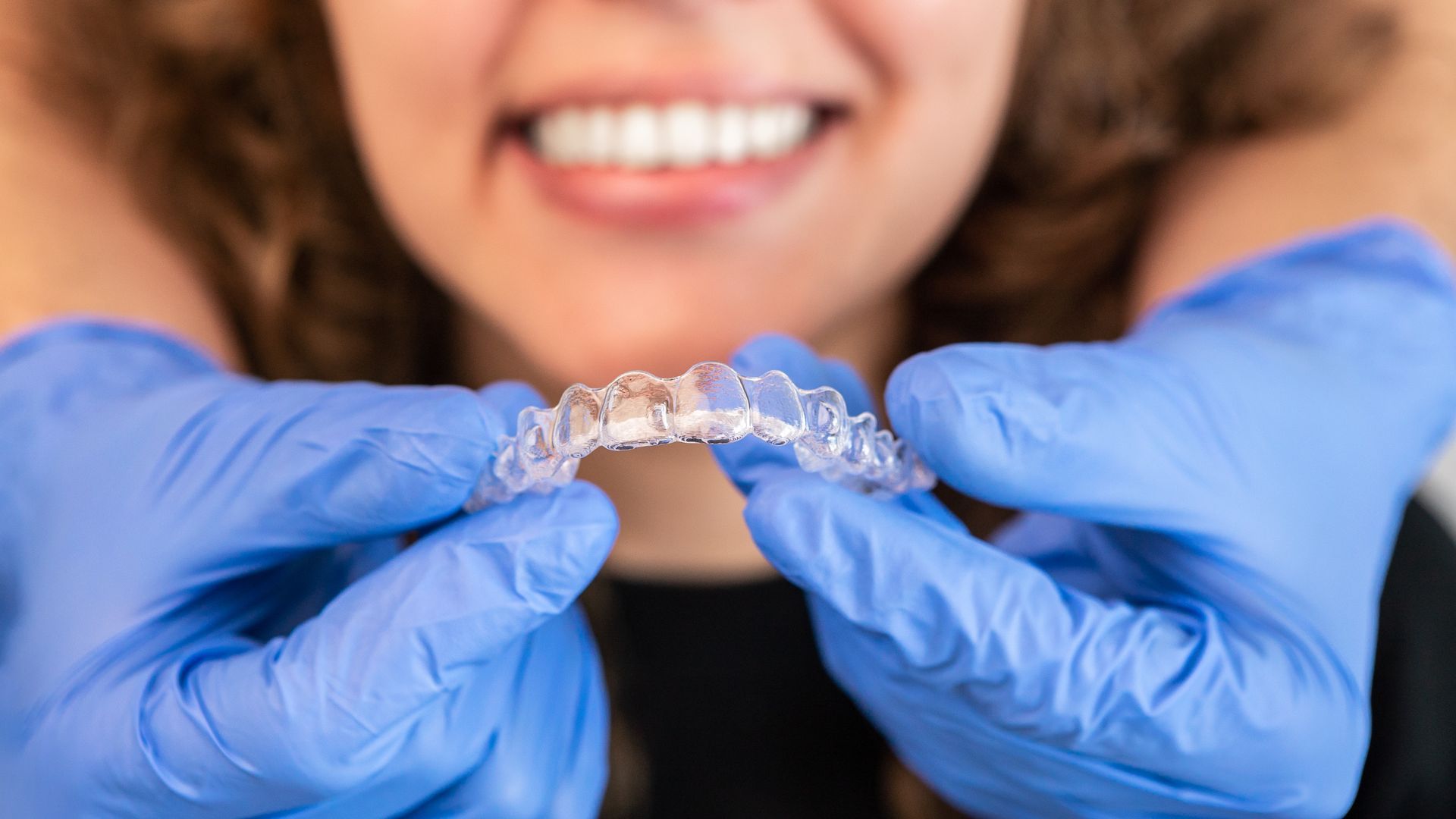 An orthodontist doctor is putting silicone invisible transparent braces on a woman's teeth.