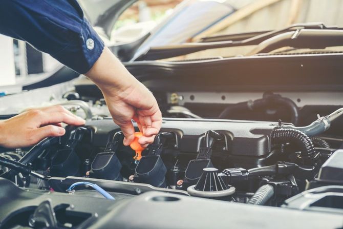 Person checking engine oil with a dipstick under an open car hood