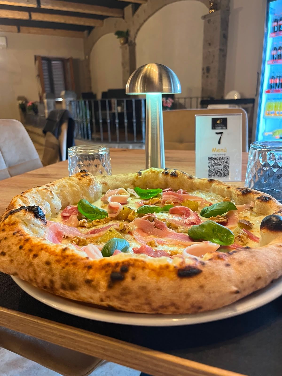 Pizza con peperoni e basilico su un tavolo di un ristorante, accanto a un espositore con codice QR per il menù.