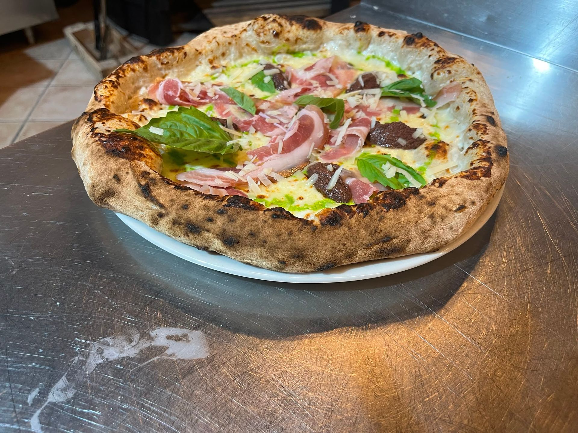 Pizza napoletana con basilico e cipolle su un vassoio di metallo appoggiato su un tavolo di legno.
