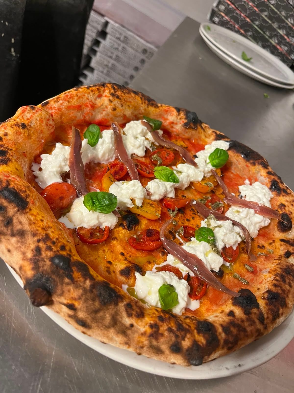Pizza margherita con basilico e fiocchi di formaggio, cotta alla griglia, servita su un piatto bianco.