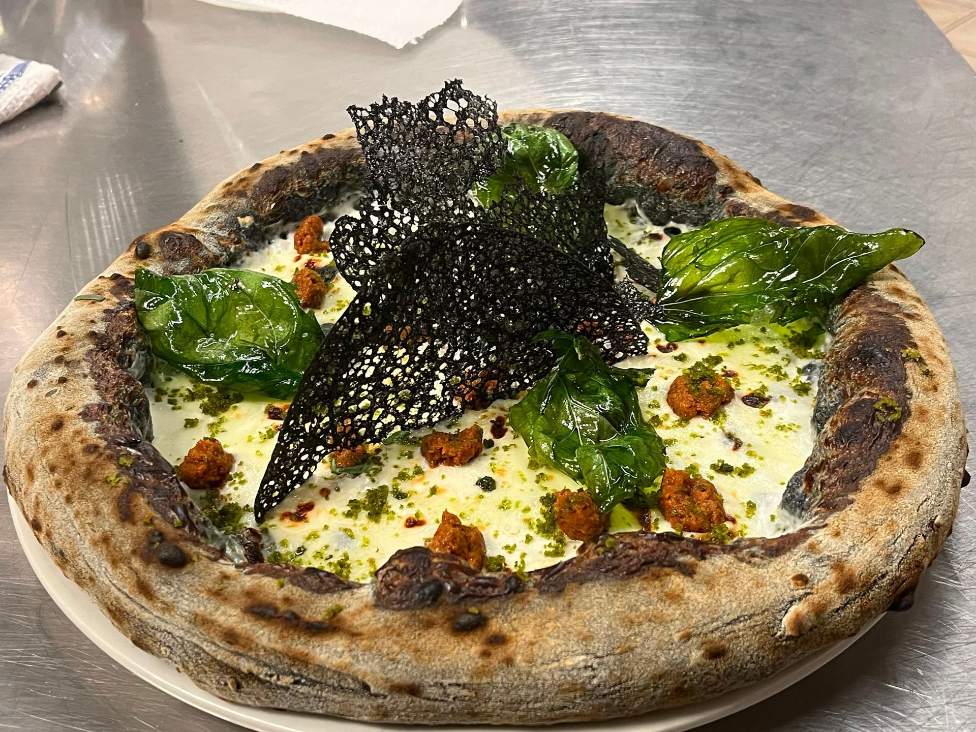 Pizza cotta nel forno a legna condita con verdure, formaggio e scaglie di tartufo nero, servita su un tavolo di metallo.