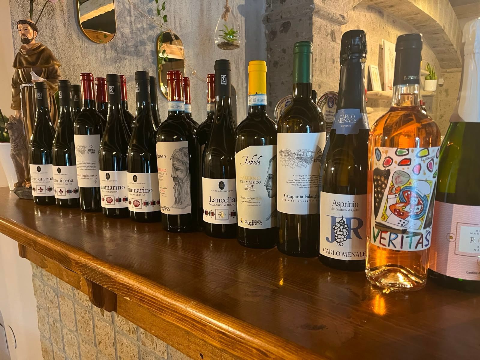 Una fila di bottiglie di vino assortite su un bancone di legno in un ambiente interno rustico.