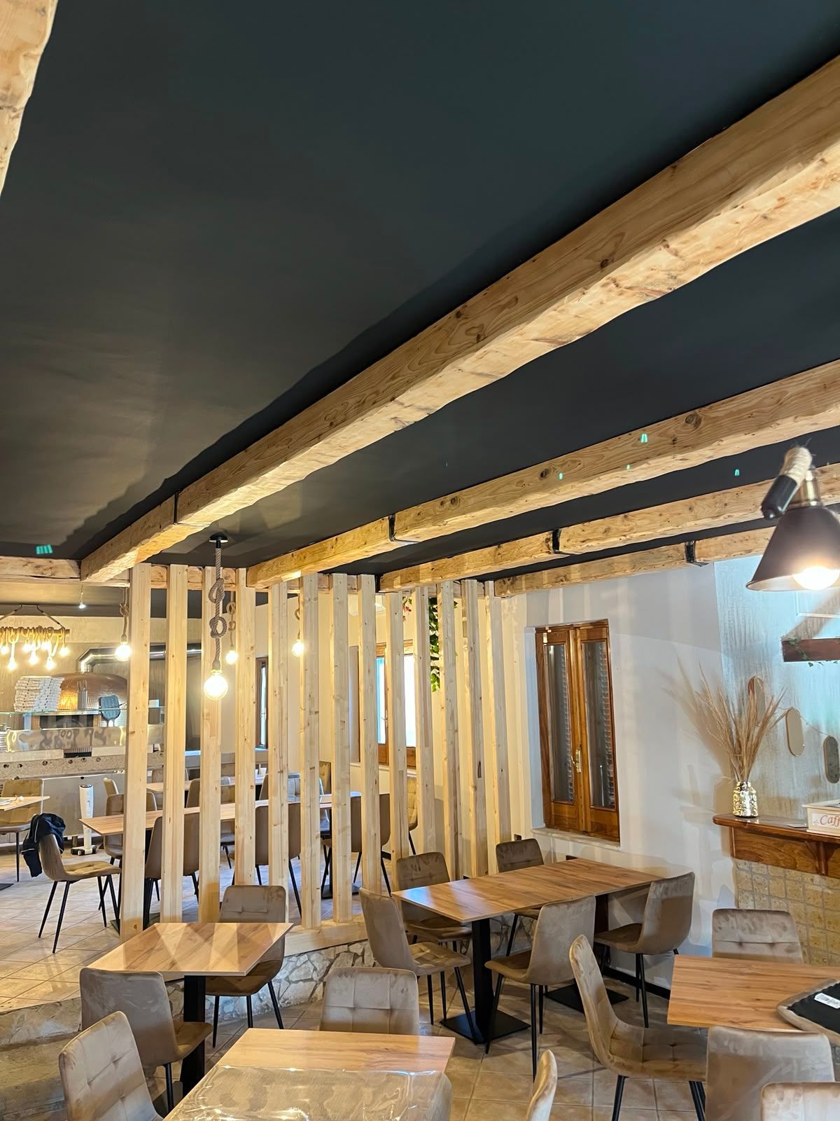 Accogliente zona salotto del caffè con tavoli e sedie in legno, doghe verticali e calde luci a sospensione.