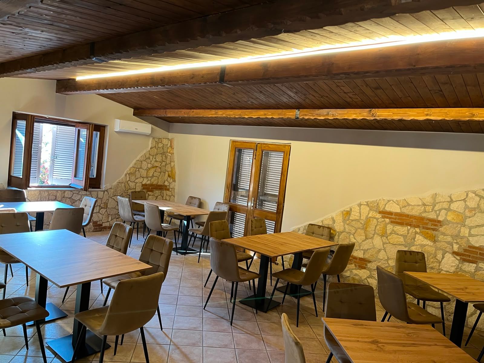 Accogliente caffè in stile rustico con travi in ​​legno, pareti in pietra e tavoli e sedie vuoti vicino a una finestra.