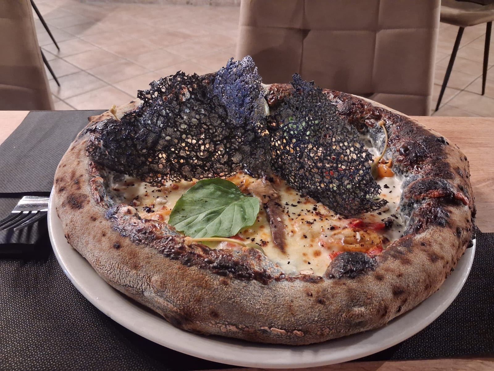 Pizza cotta nel forno a legna con crosta bruciacchiata, formaggio fuso, guarnizione al tartufo nero e basilico su un piatto