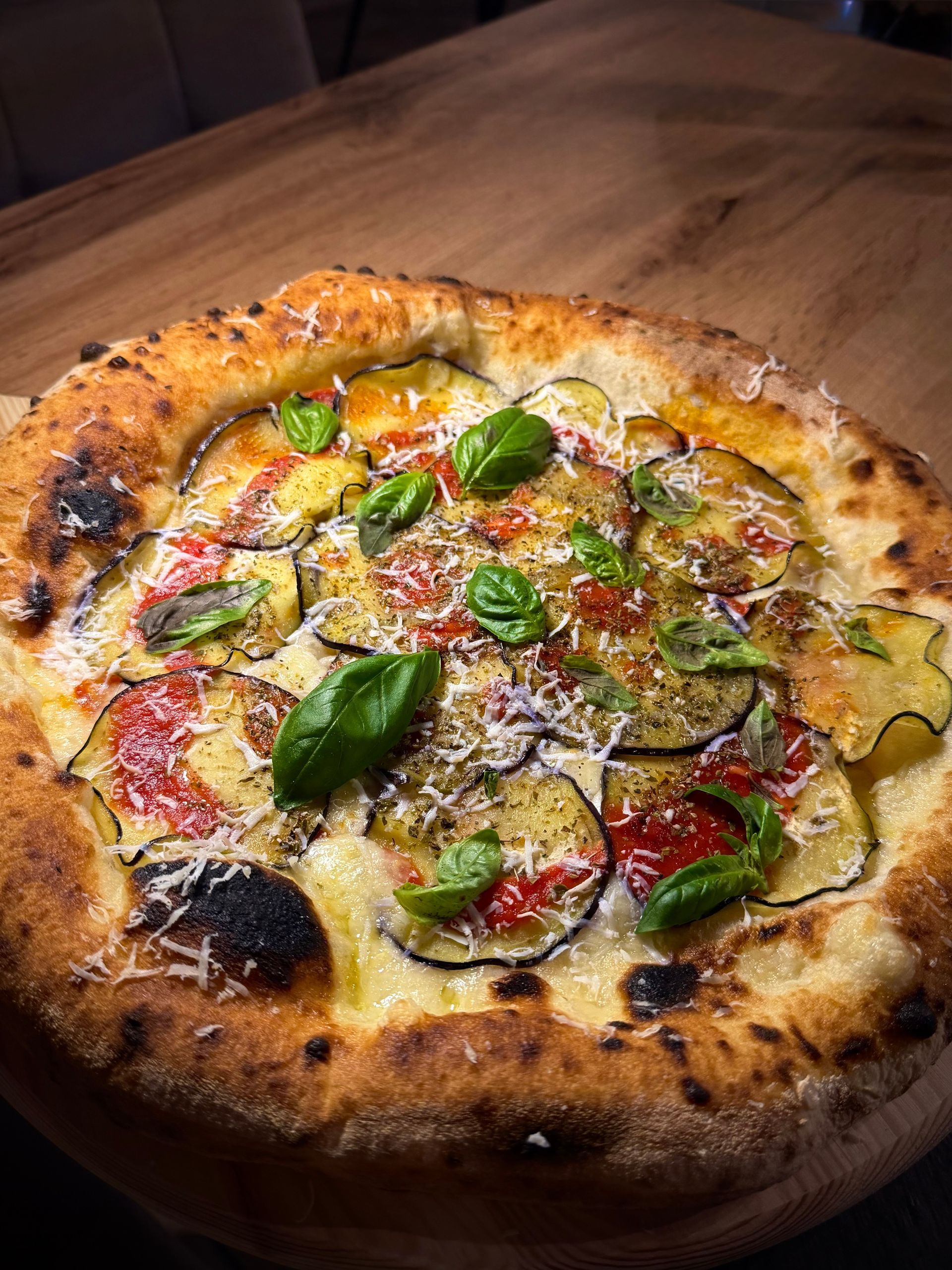 Pizza cotta nel forno a legna con basilico, pomodori e formaggio fuso su un tagliere di legno.