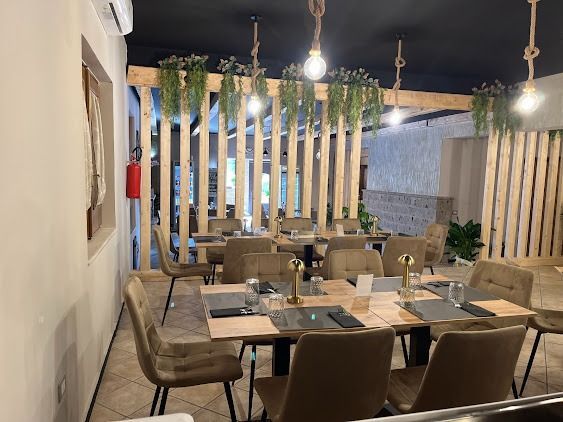 Interni moderni di un ristorante con tavoli in legno, sedie color cuoio, lampade a sospensione e piante rampicanti.