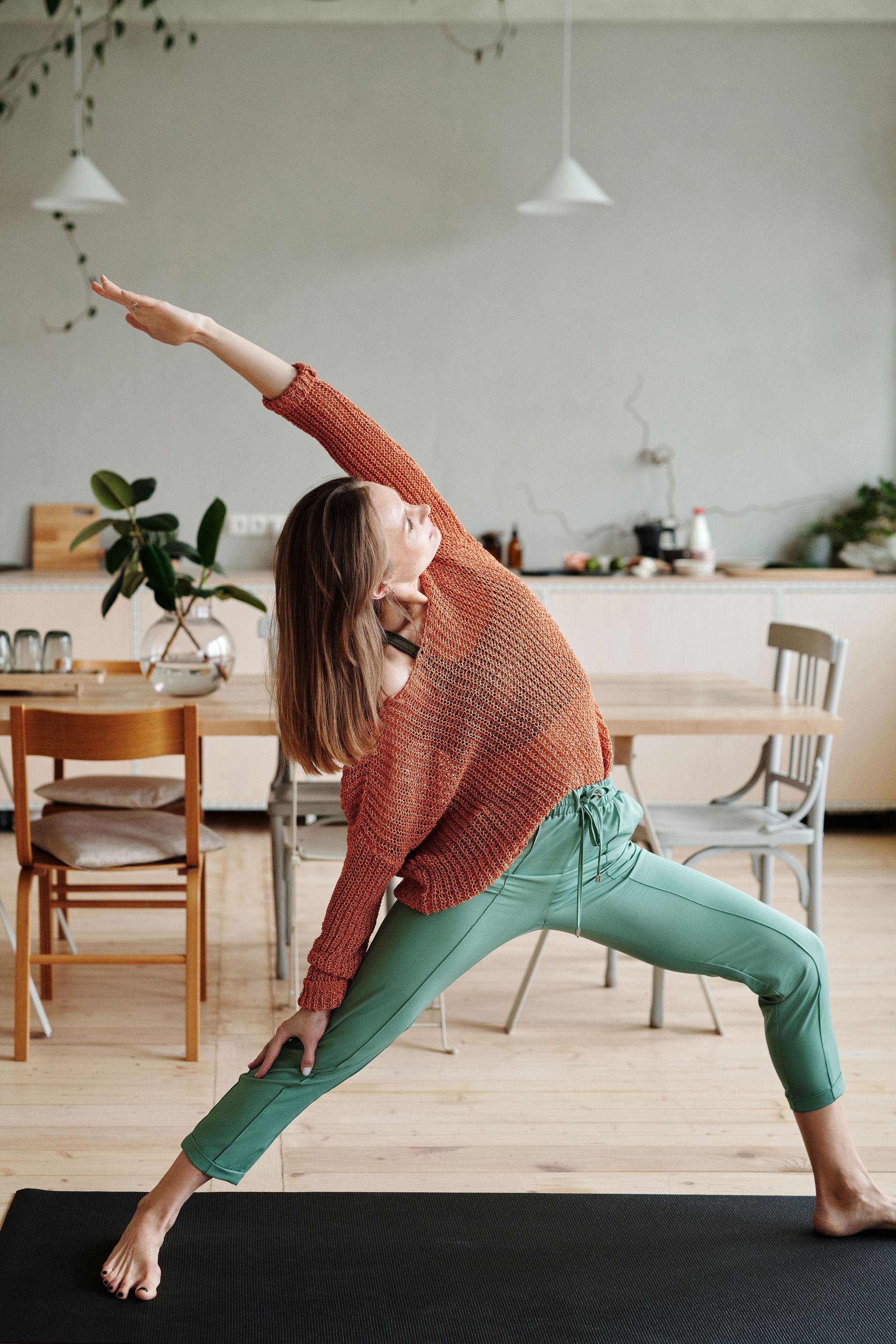 Person doing a pilates on a black mat in a bright living room.