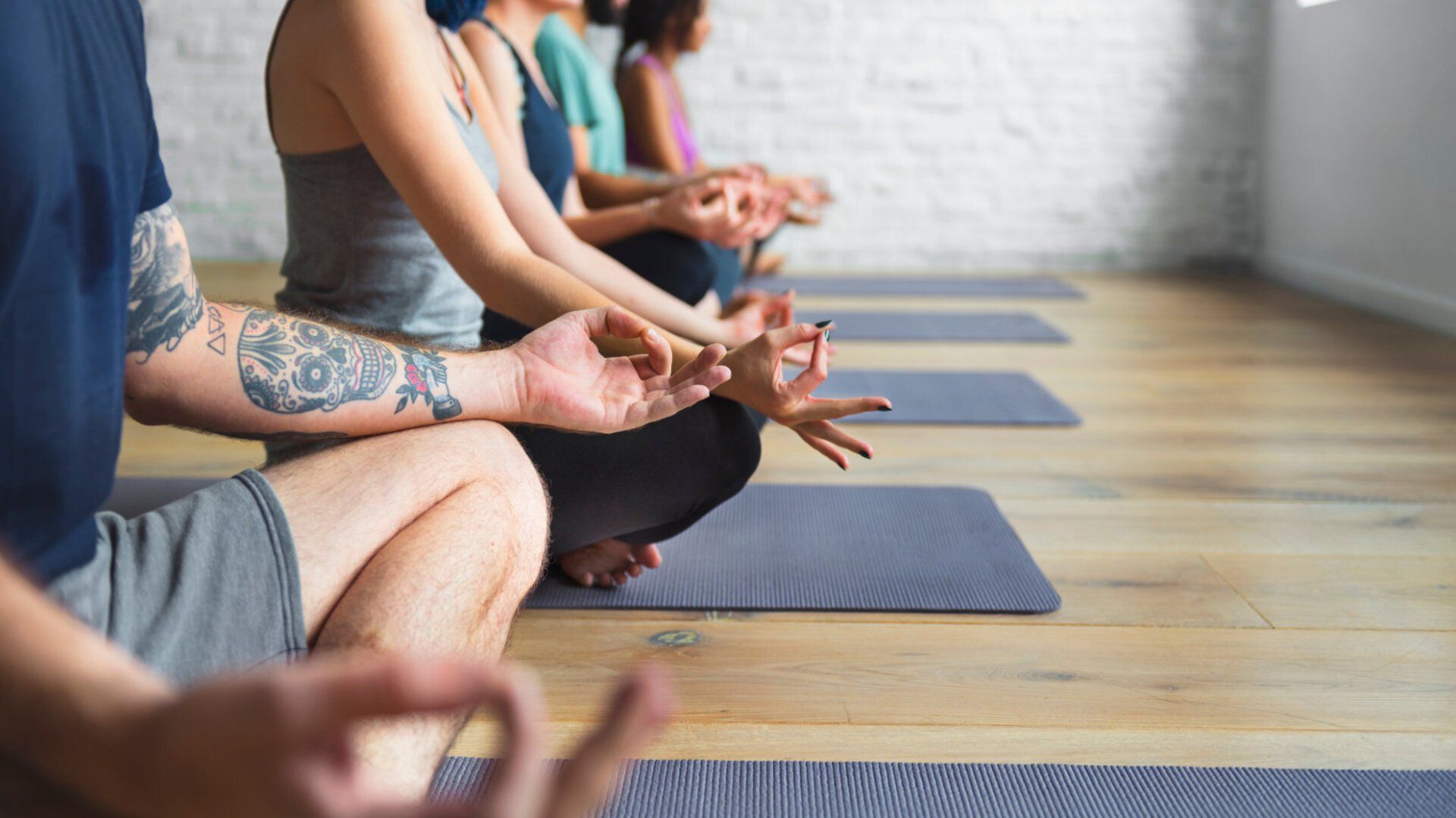 A group of people are sitting in a row on yoga mats in a yoga studio.