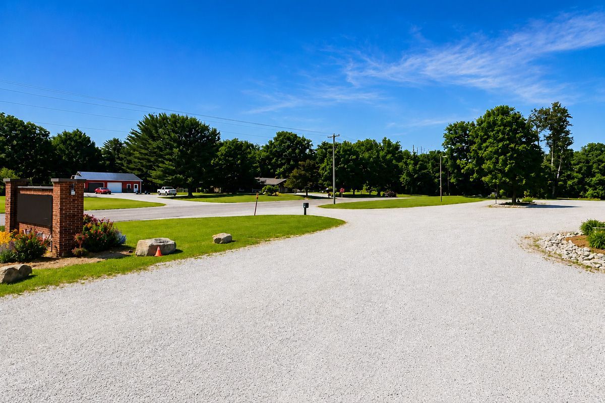 Gravel driveway curving through a green park with trees, grass, and a clear blue sky