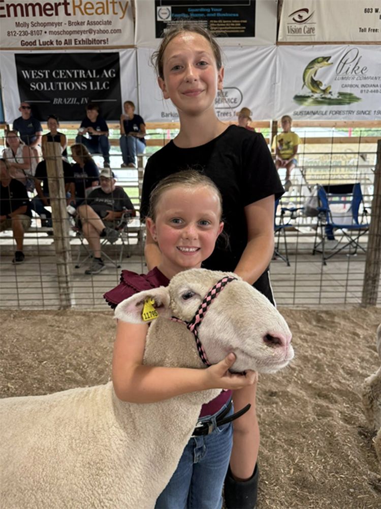 Girl in black shirt posing with a sheep at a livestock show inside a barn.