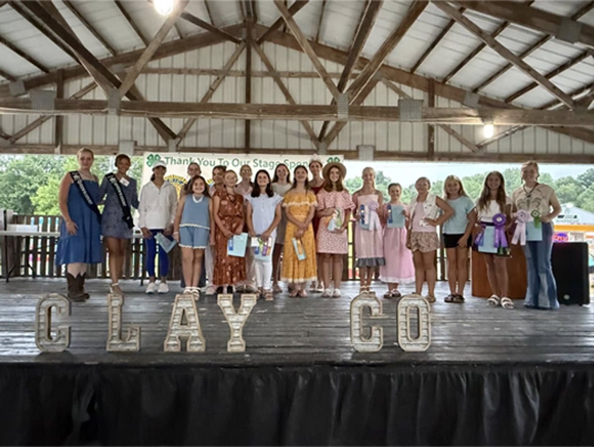 Group standing on stage under a pavilion, holding giant letters spelling “CLAY GO”
