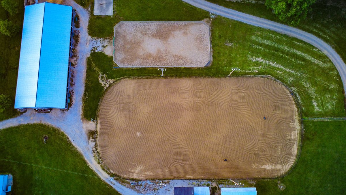 Aerial view of a dirt oval track with a small blue-roofed building and grassy fields around it