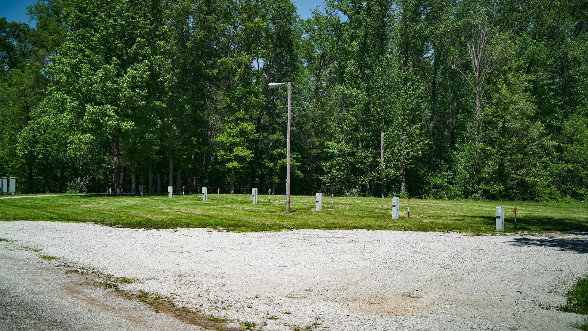 Gravel clearing with a lamppost and short white posts beside a grassy tree line