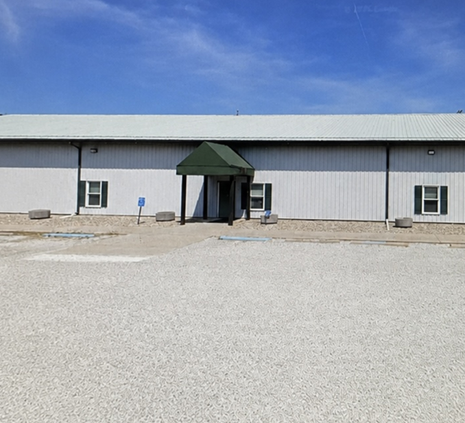 Single-story gray building with a green awning and gravel lot under a blue sky