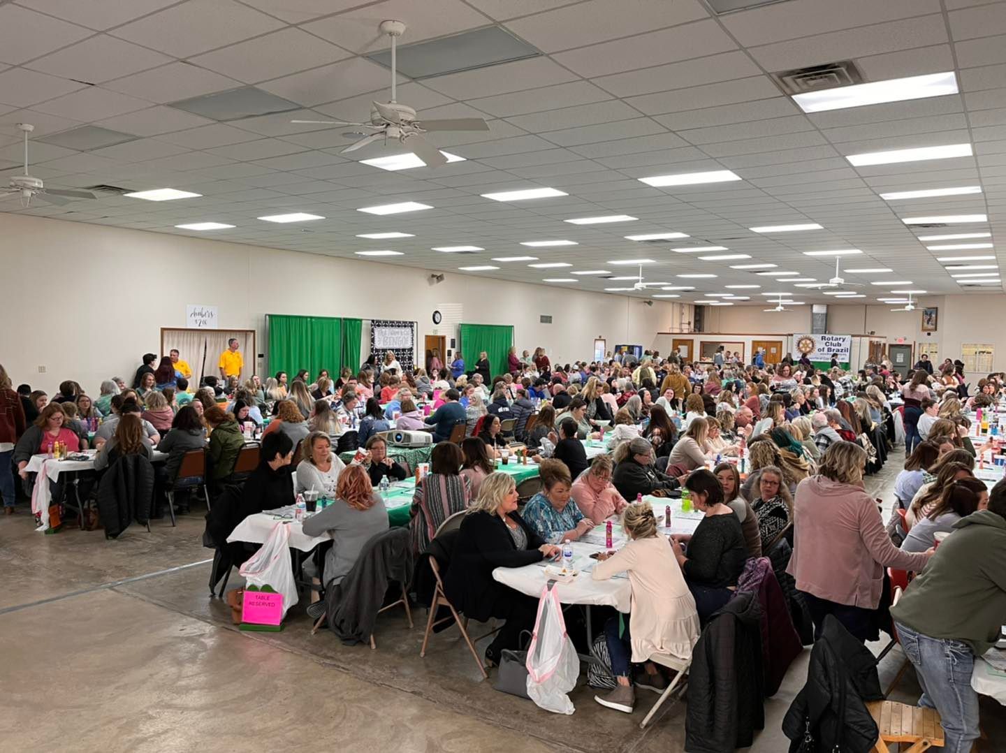 Large banquet hall filled with people seated at round tables during a community gathering or event