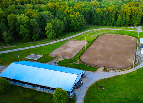 Aerial view of a baseball field and adjacent covered building beside a tree-lined road